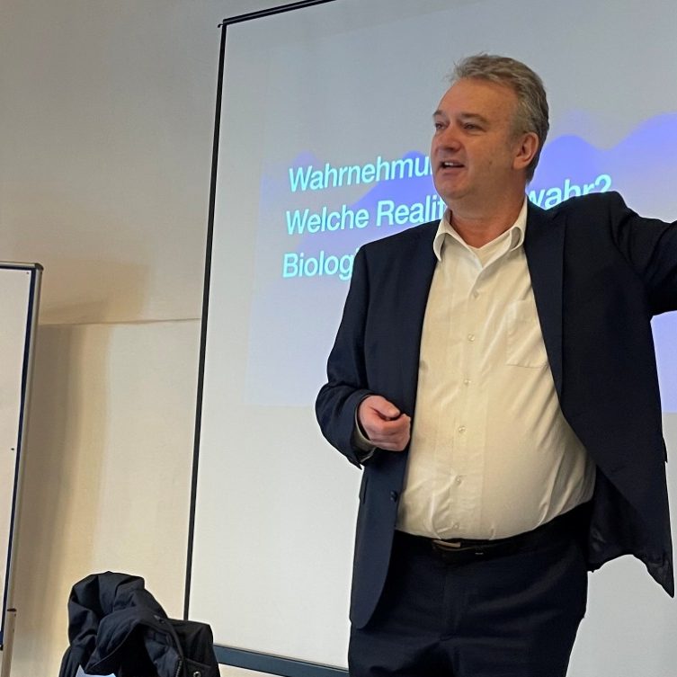 Joachim Skrambraks bei einem Vortrag Mann in Anzug erklärt etwas vor einer Präsentationstechnik im Seminarraum.